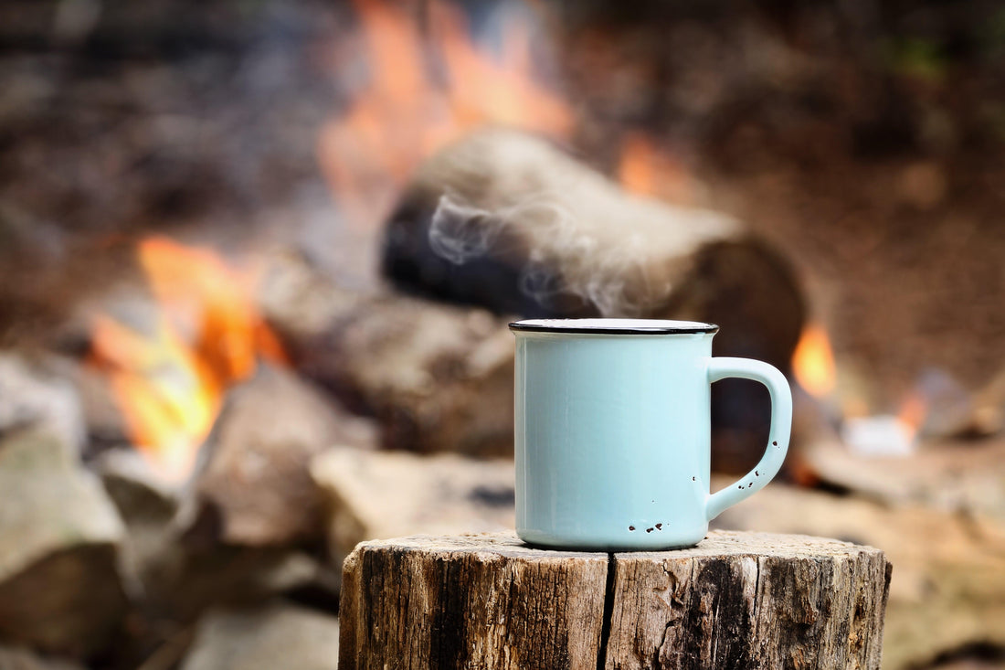 A chipped blue mug sitting on a log in front of an outdoor campfire