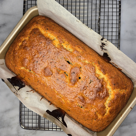 A golden brown tea cake in a loaf pan sitting on a wire rack